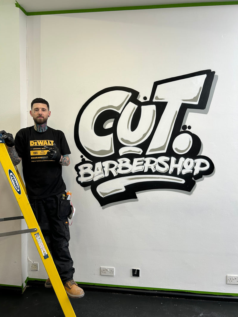 Person leaning against a yellow safety barrier with a 'Cut Barbershop' sign on the wall.
