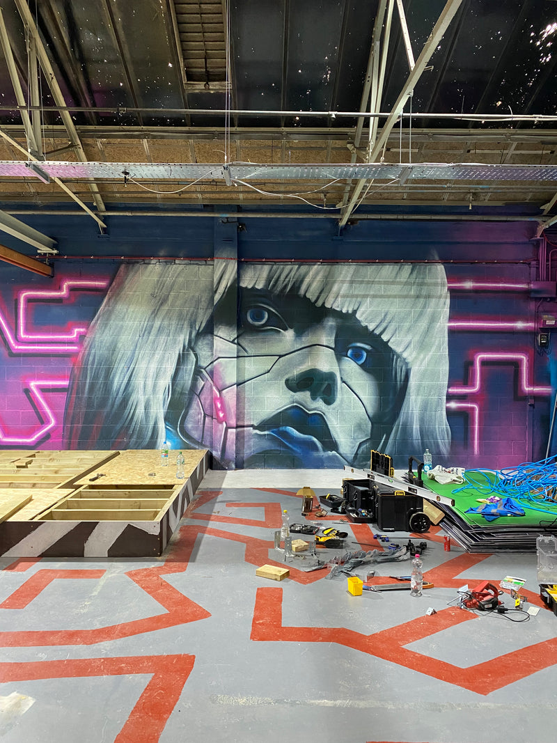 Mural of a stylized face on a wall with neon lights and geometric shapes.