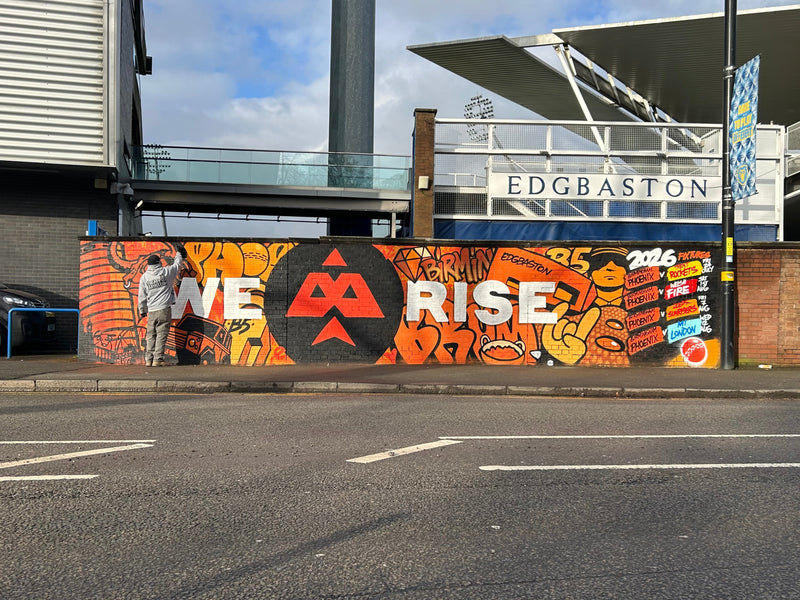 Mural with 'WE RISE' on a wall at Edgbaston cricket ground.