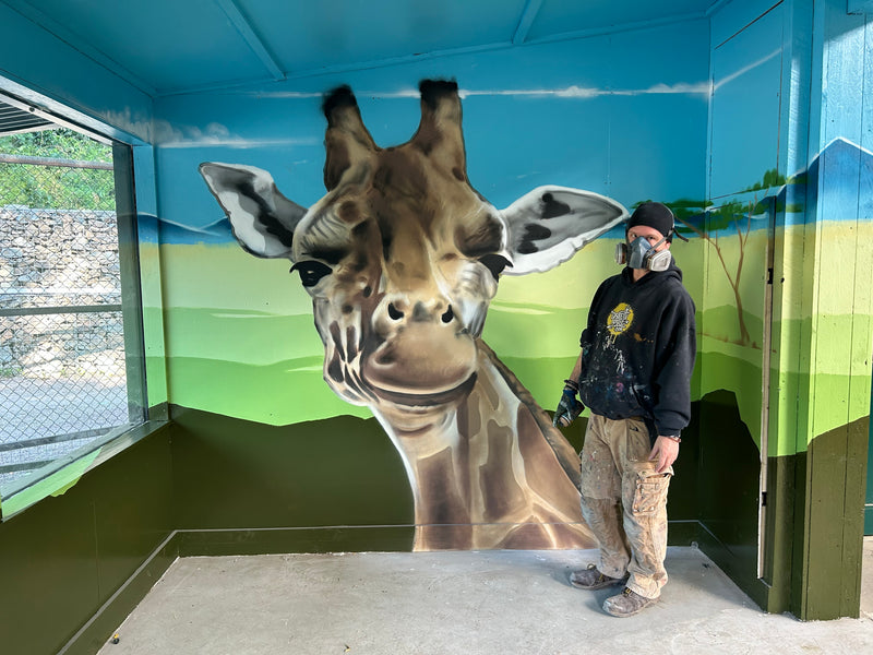 Person standing next to a large giraffe mural in an indoor setting