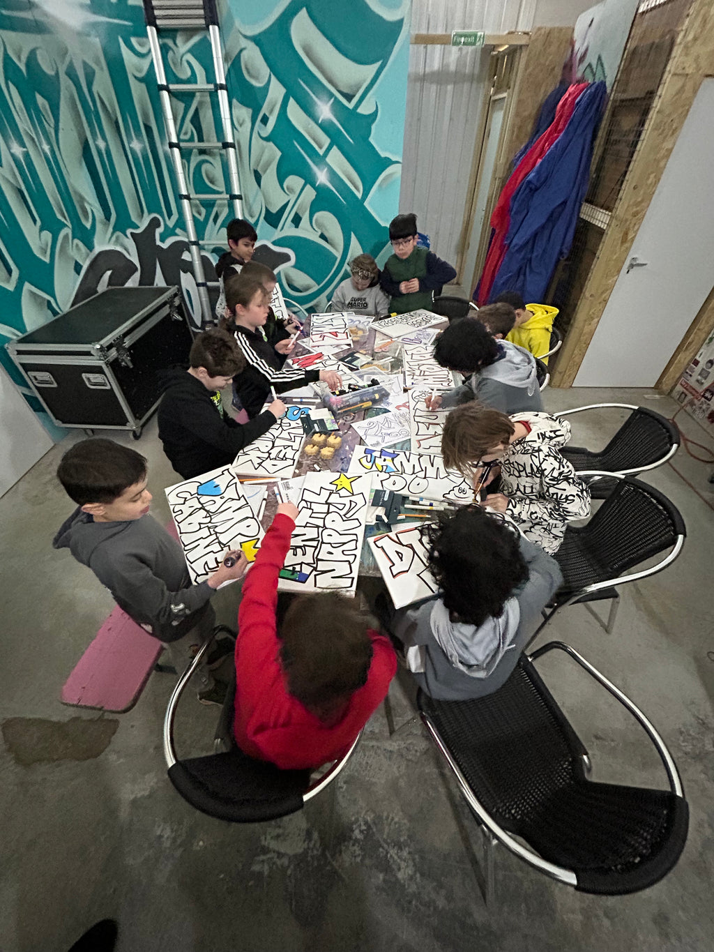 Group of people colouring graffiti canvases in a casual setting with colorful walls and furniture.