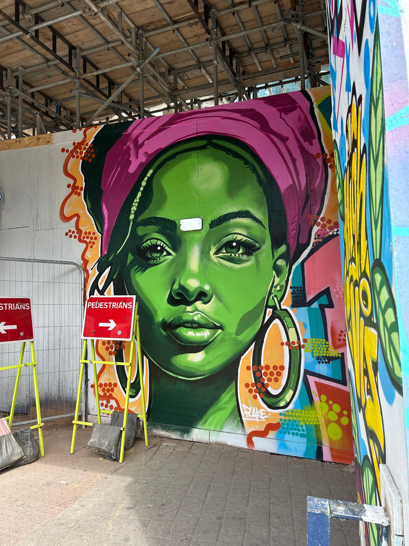 Colorful mural of a green-skinned figure with a purple hood on a building facade.