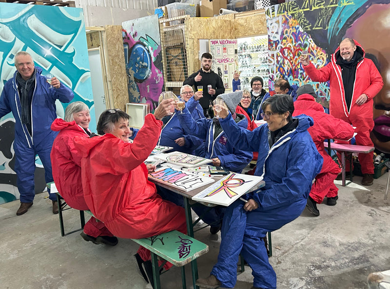 Group of people in colorful outfits in a room with art supplies and artwork.