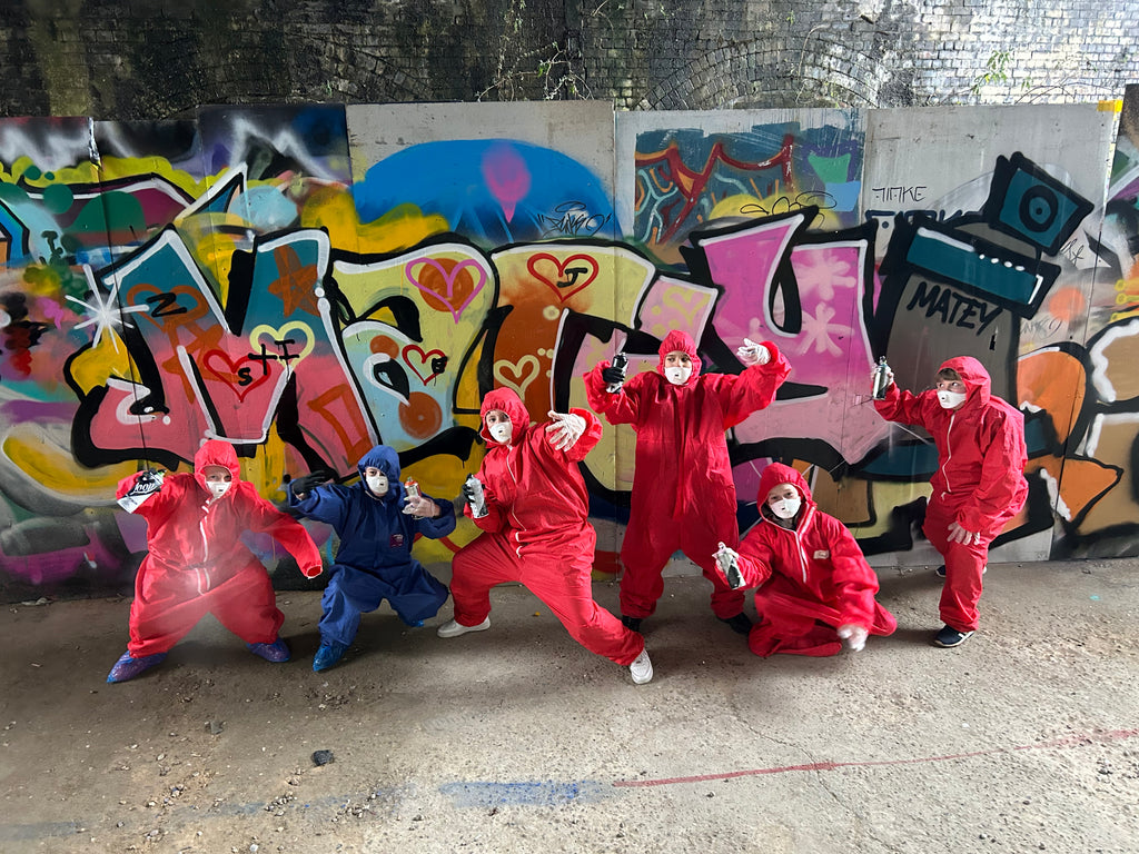 Group of people in colorful outfits posing in front of a graffiti-covered wall.