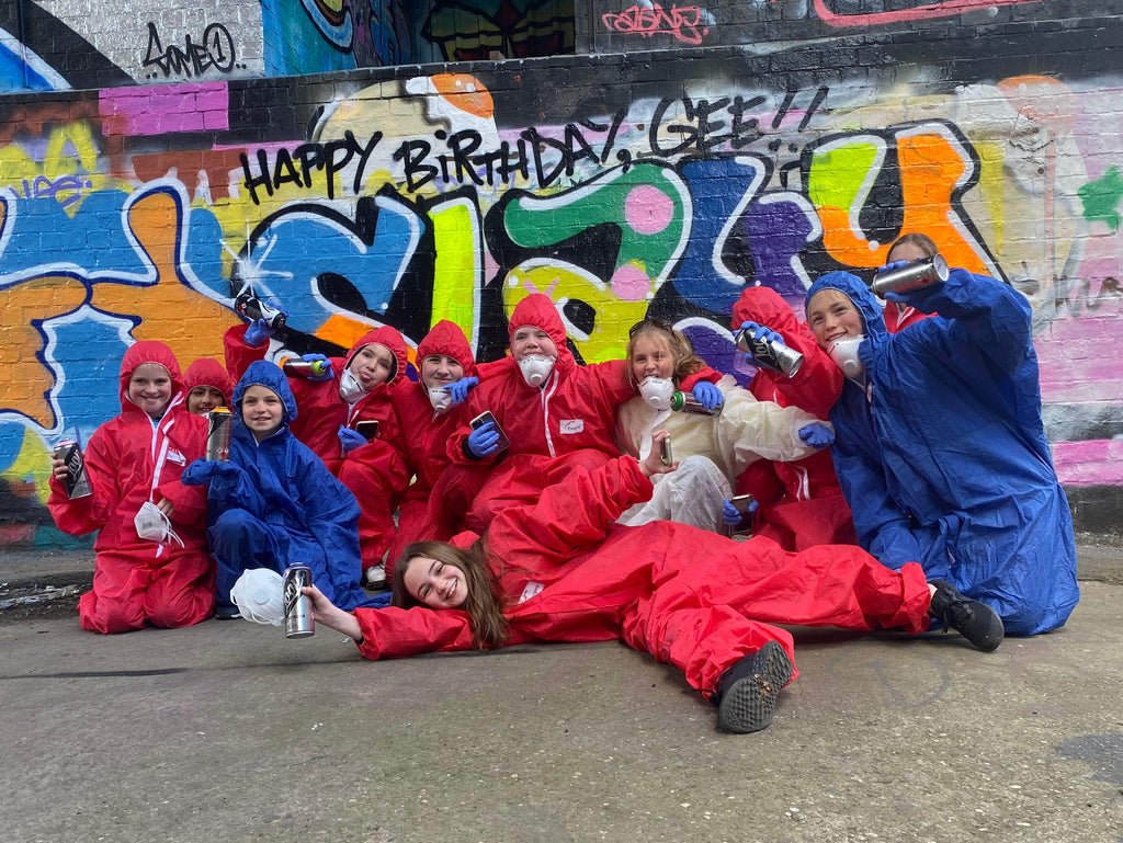 Group of people in colorful outfits posing in front of a graffiti-covered wall.