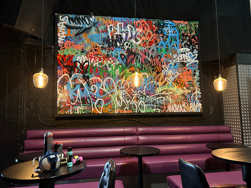 Graffiti-style artwork on a wall in a modern interior setting with purple seating and round tables.
