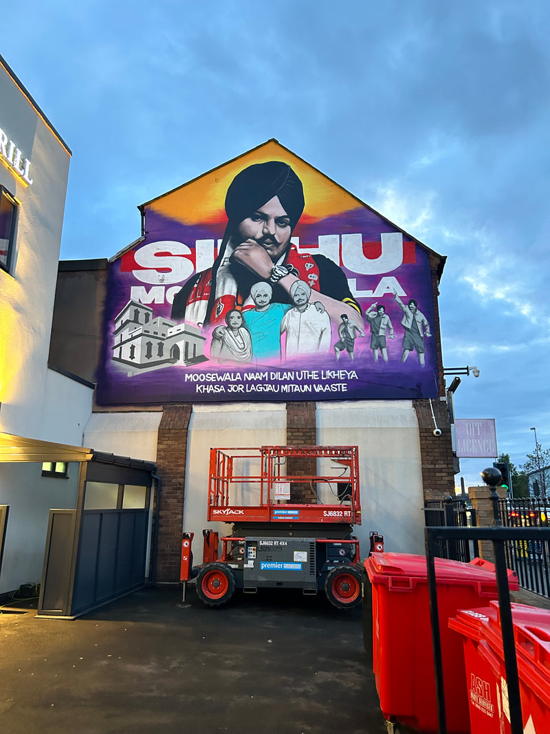 Large outdoor mural with Sidhu moose wala holding a microphone against a blue sky.