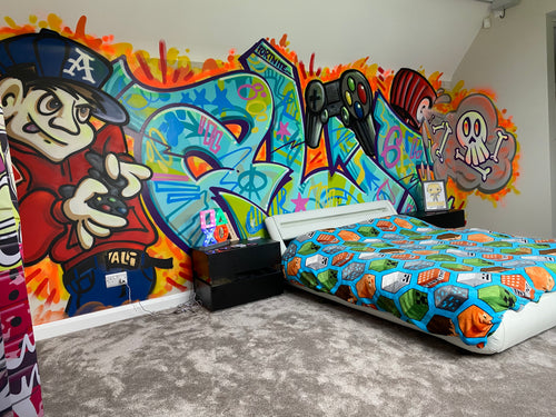 A bedroom with a colorful graffiti piece on the walls featuring various characters and text.